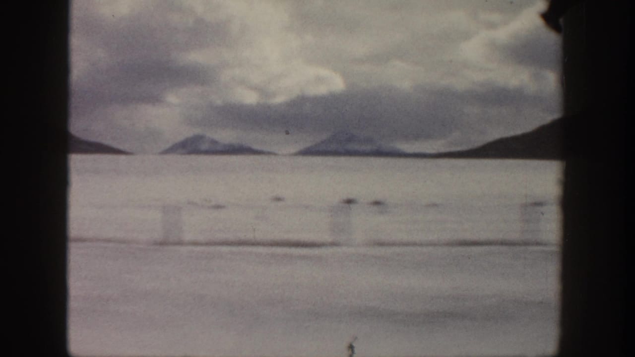 1961 Aspen-area home-movie view of distant mountains and water under a cloudy sky, framed by dark 8mm gate edges.