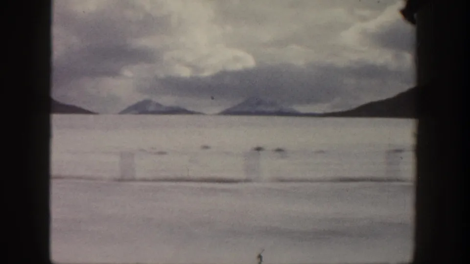 1961 Aspen-area home-movie view of distant mountains and water under a cloudy sky, framed by dark 8mm gate edges.