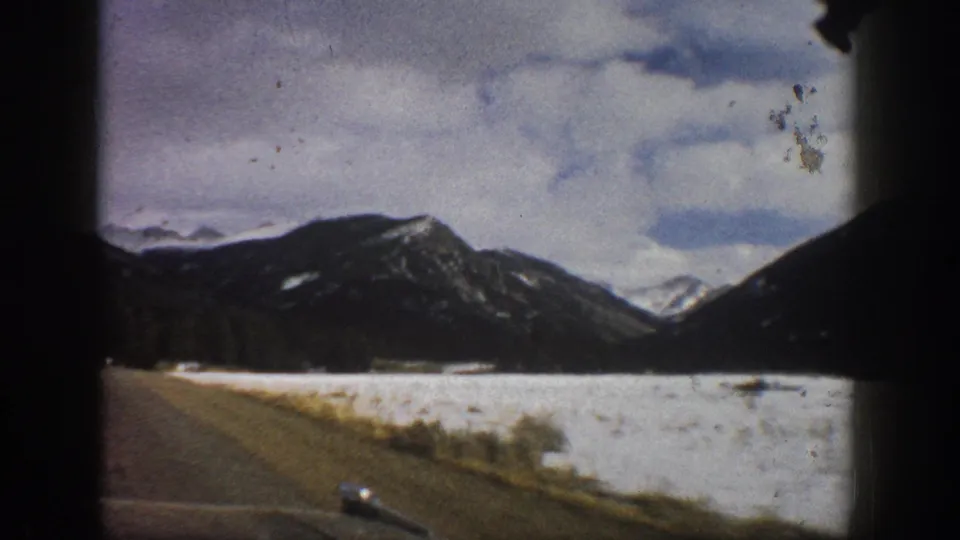 Final 1961 Aspen road-view frame with snowy foreground, dark mountains, clouds, and visible 8mm film wear.