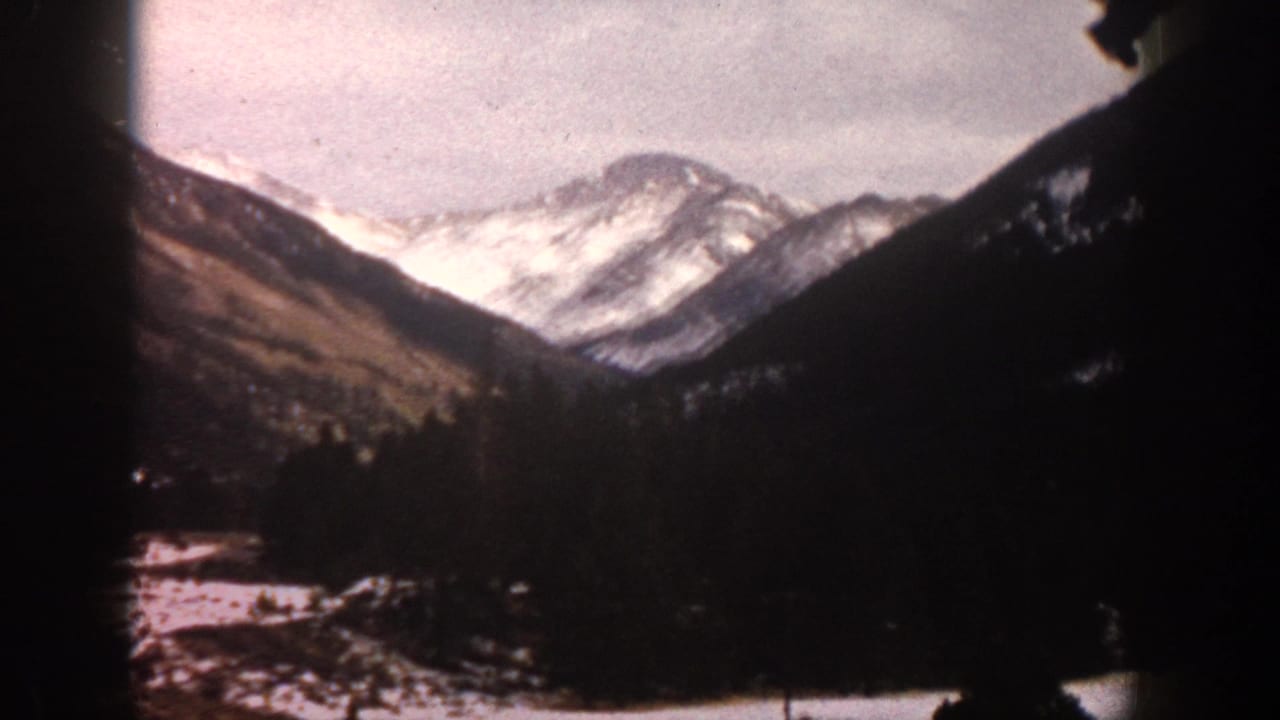 1961 Aspen, Colorado 8mm frame showing snow-covered peaks, forested slopes, and a partially snowy valley floor.
