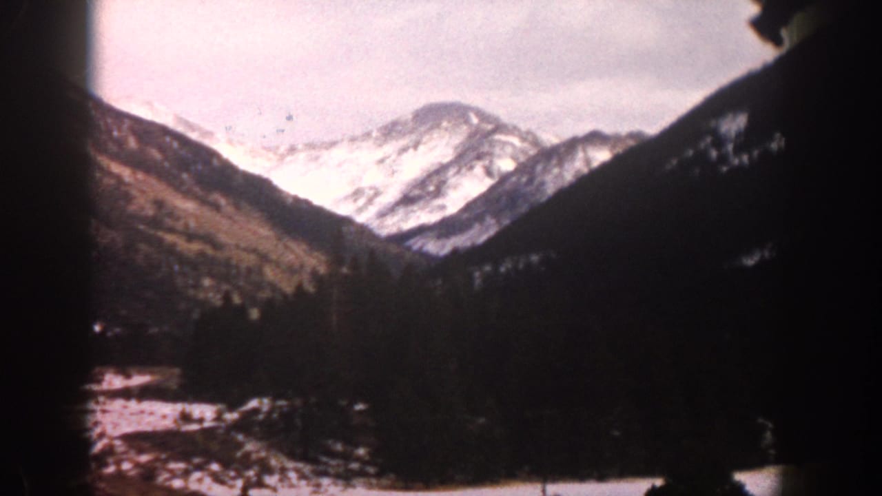 Snow-covered mountain range with dark forested hillsides and snow in the lower valley.