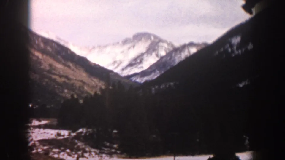 Faded 1961 Aspen, Colorado 8mm frame showing bright snowy peaks, dark trees, and visible film border shadows.