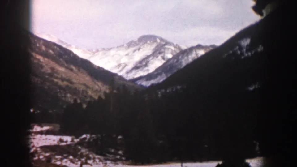1961 Aspen, Colorado scenic frame with snow-covered peaks, forested valley sides, and warm faded 8mm color.