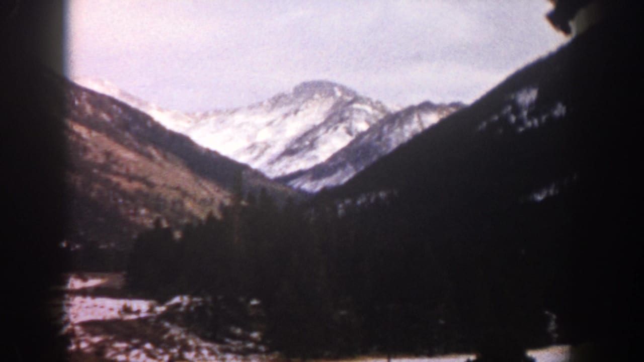 1961 Aspen-area 8mm frame showing snow-capped mountains and a dark valley viewed from inside or near a moving car.