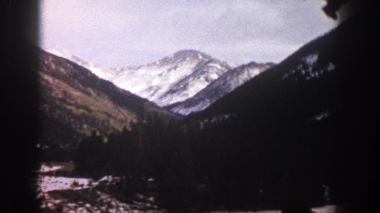 Aspen, Colorado home-movie frame with snow-bright peaks, wooded slopes, and heavy 8mm gate-edge shadows.