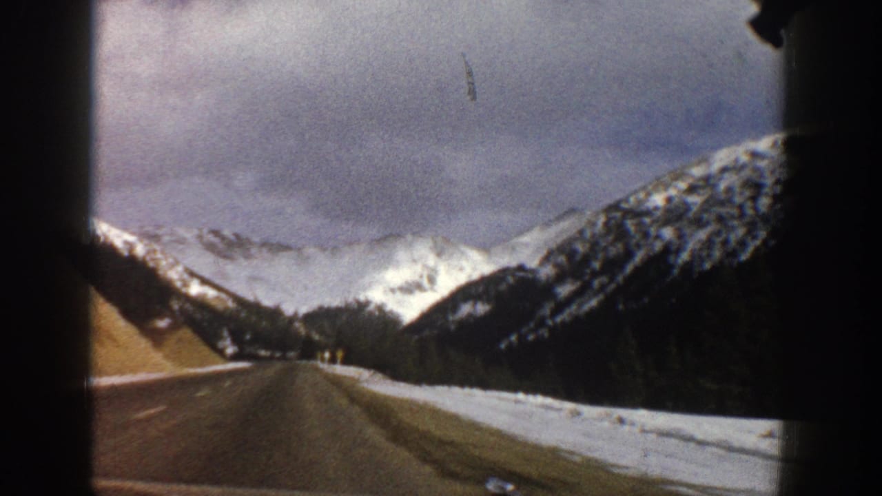 A car-window view of a winter road near Aspen, Colorado, with snow on the roadside and bright mountain peaks beyond.