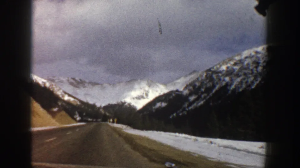 A car-window view of a winter road near Aspen, Colorado, with snow on the roadside and bright mountain peaks beyond.