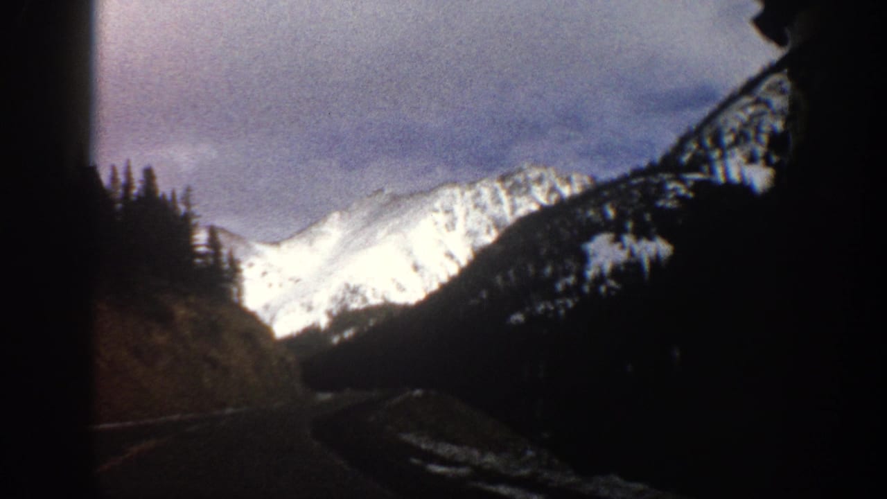Snowy Colorado mountain terrain appears ahead from a moving 8mm travel view near Aspen in 1961.