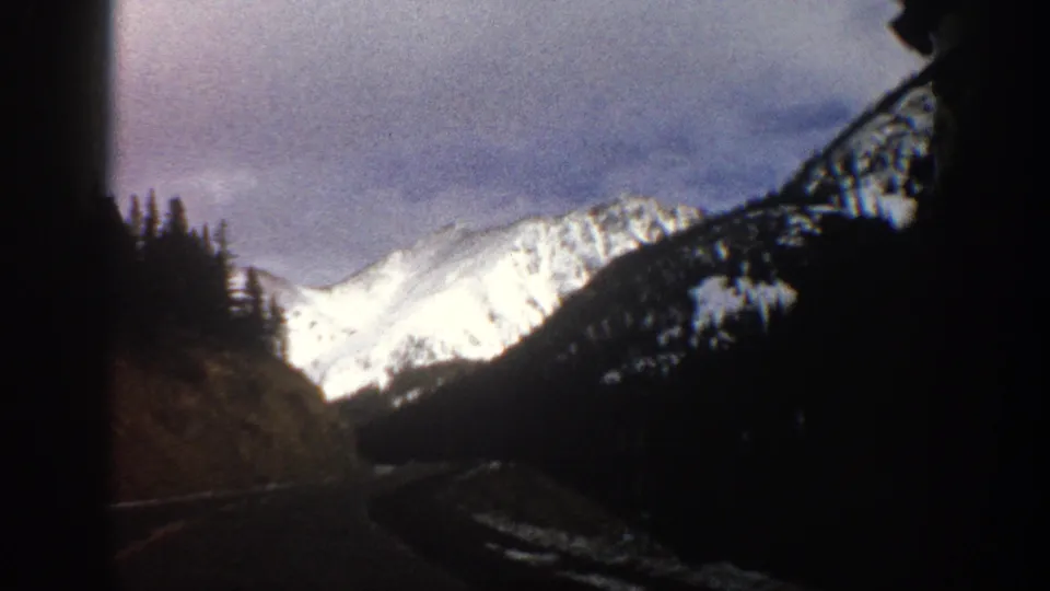 Snowy Colorado mountain terrain appears ahead from a moving 8mm travel view near Aspen in 1961.