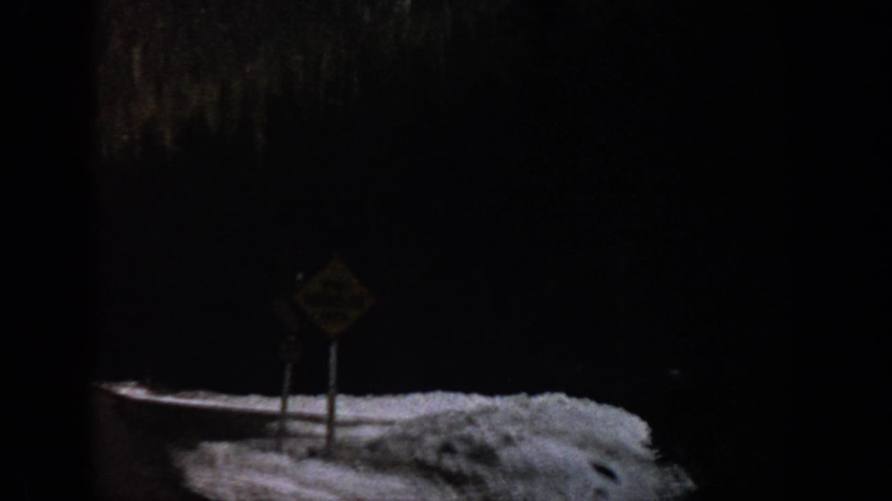 Snowy roadside warning sign seen from inside a dark vehicle frame.