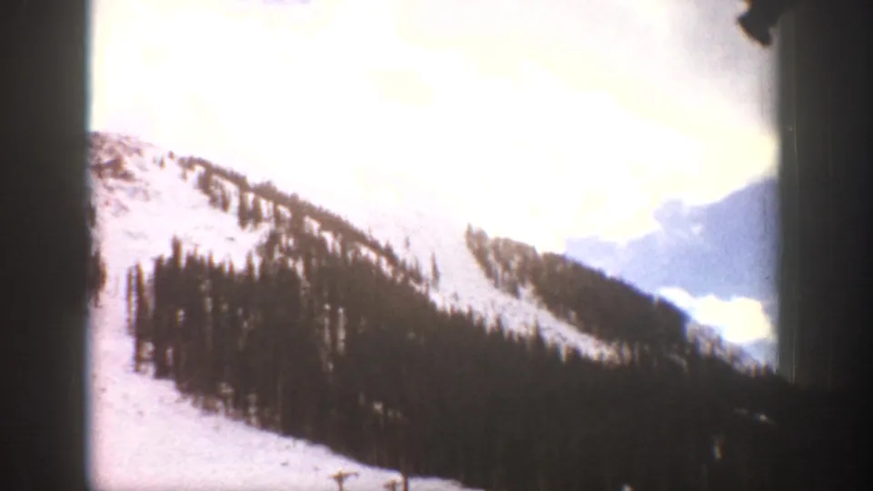 1961 Aspen-area 8mm view of a snowy mountain slope, tree stands, and bright clouded sky.