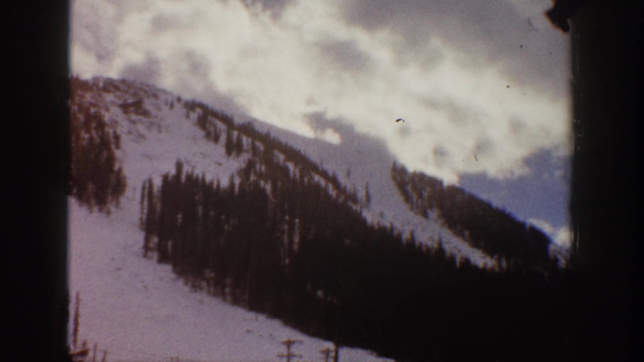 1961 Aspen, Colorado 8mm frame showing a snowy mountain slope with dark evergreen trees and an overcast sky.