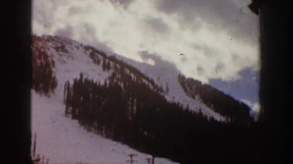 1961 Aspen, Colorado 8mm frame showing a snowy mountain slope with dark evergreen trees and an overcast sky.