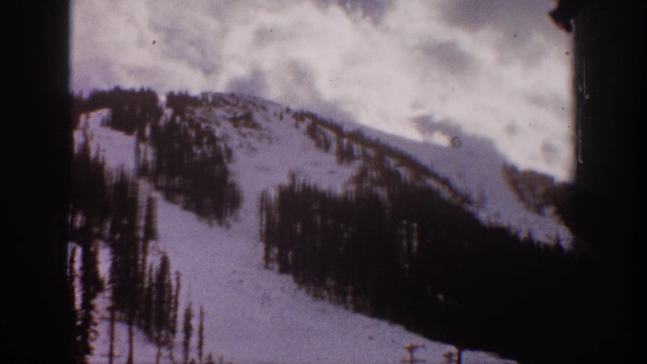Snowy ridgeline and evergreen-covered slope framed by dark film edges.