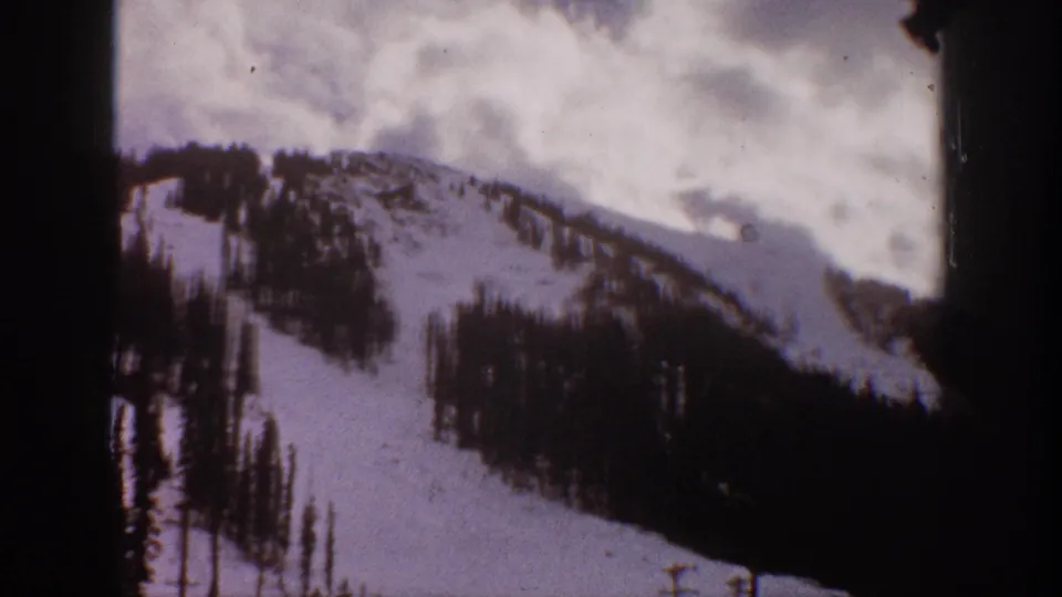 1961 Aspen, Colorado home-movie frame of a snow-covered ridge with evergreen patches and visible 8mm frame borders.