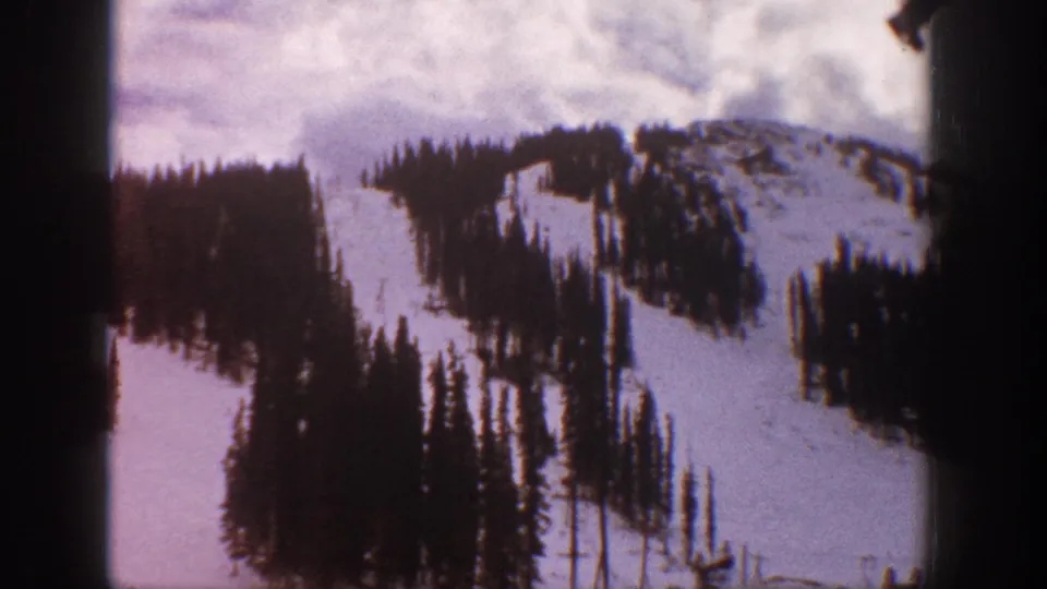 1961 Aspen, Colorado 8mm frame of a snowy mountain slope, evergreen clusters, cloudy sky, and dark edge shading.