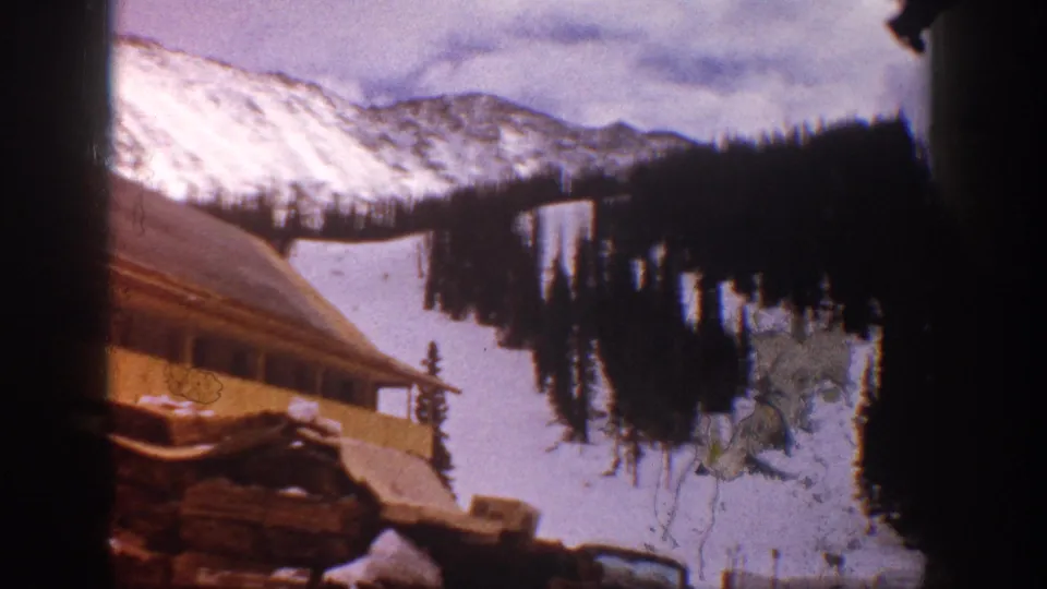 Aspen, Colorado 1961 8mm frame with a wooden lodge roof, snow-covered runs, evergreens, and distant mountain ridges.