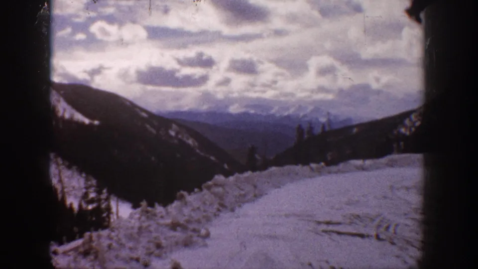 Aspen home-movie frame showing a snow-covered road edge and layered mountain views under a cloudy winter sky.