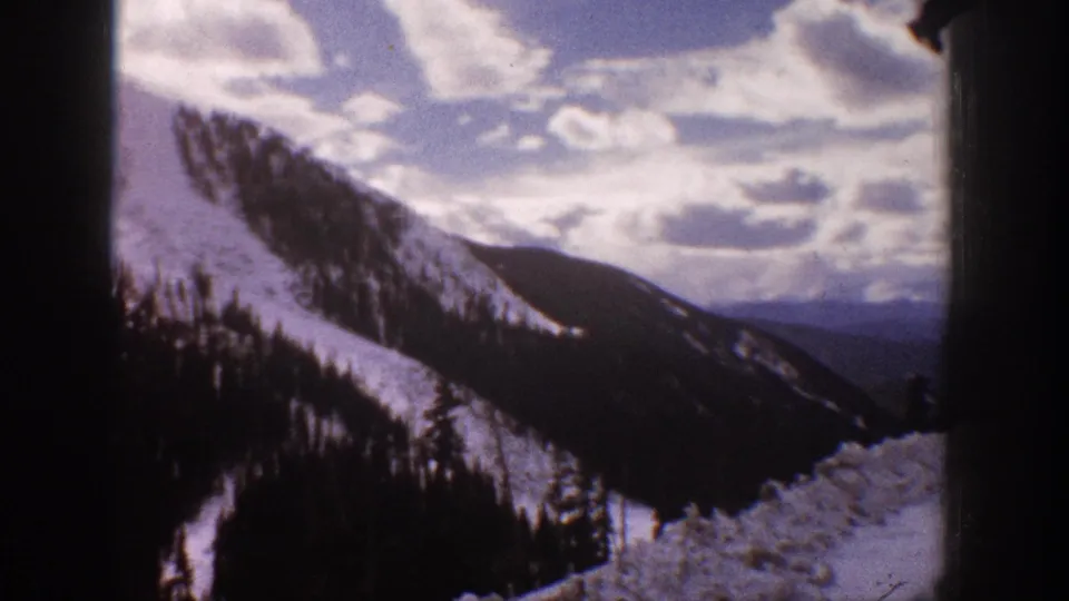 1961 Aspen, Colorado home-movie view of a snowy mountainside, evergreen stands, and hazy ridges beyond.