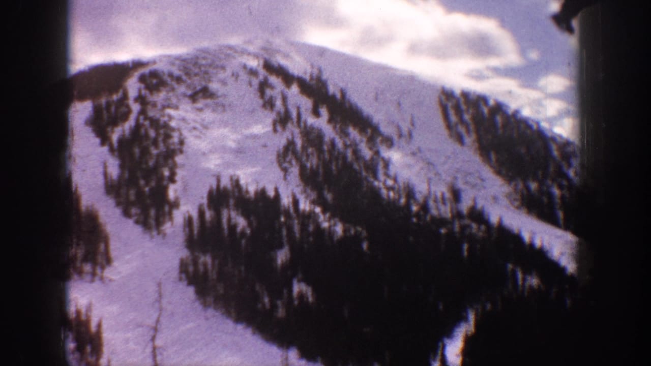 Snowy ridge and evergreen-covered slope seen through a dark vertical film edge.