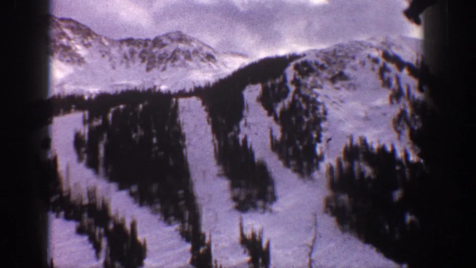 1961 Aspen, Colorado 8mm view of snowy ridges, clustered evergreen forests, exposed slope contours, and bright cloud cover.