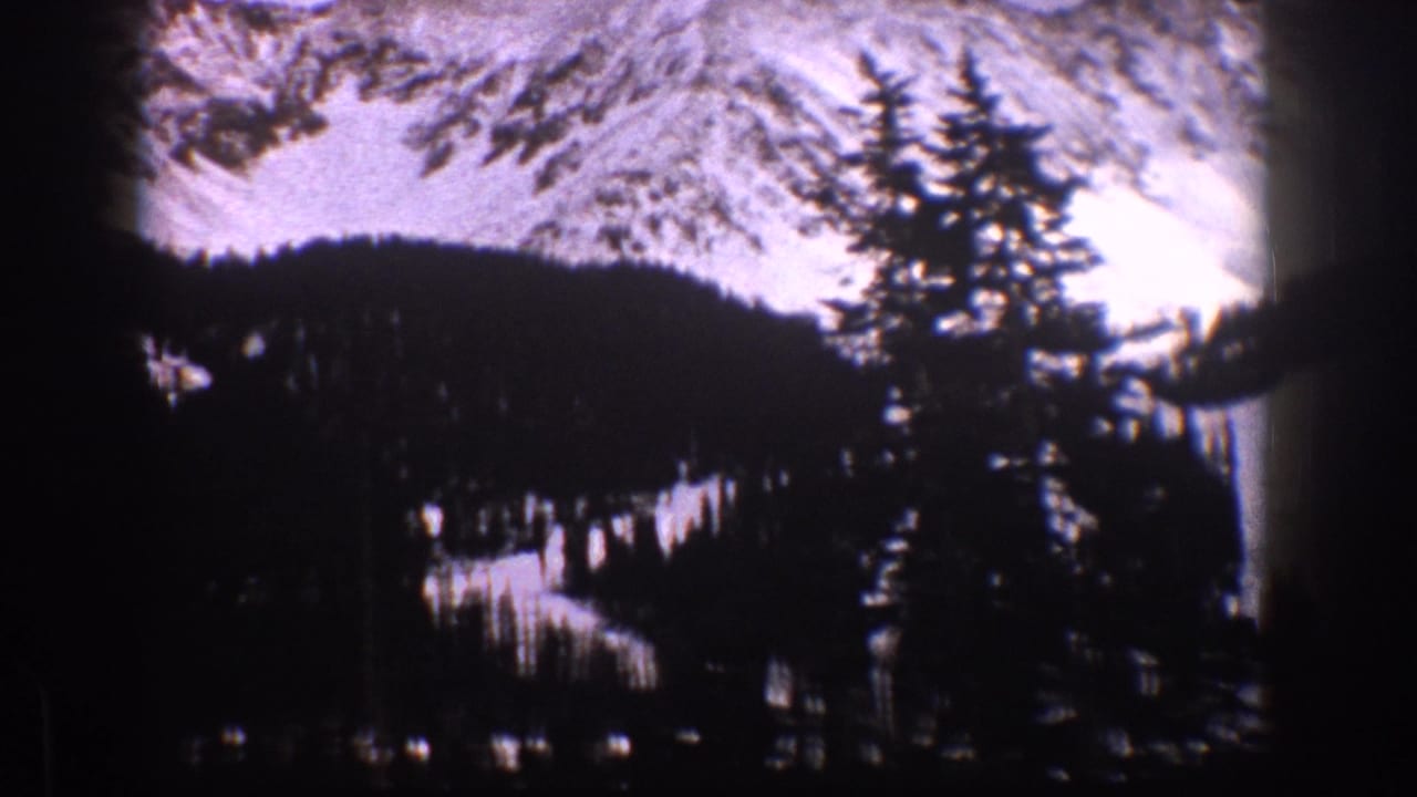 1961 Aspen, Colorado home-movie view of snow-covered mountains rising behind dense evergreen trees.