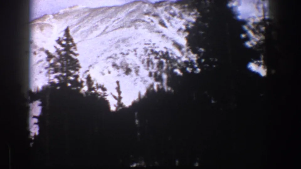 1961 Aspen, Colorado landscape frame showing a snowy ridge framed by tall evergreen silhouettes.