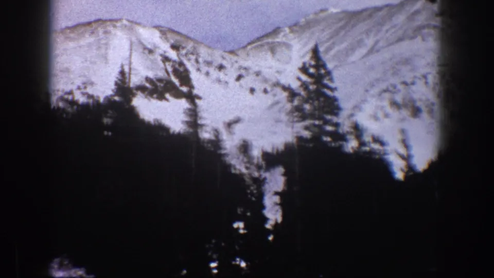 1961 Aspen, Colorado frame with a bright snow-covered mountain face and dark conifer silhouettes in front.