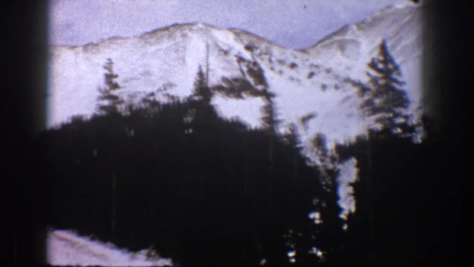 1961 Aspen, Colorado home-movie view of a snowy slope beyond a shadowed stand of evergreens.
