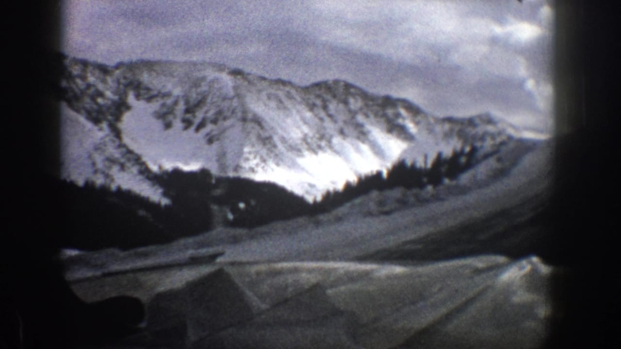 Snowy mountain range with dark tree line and foreground road area.