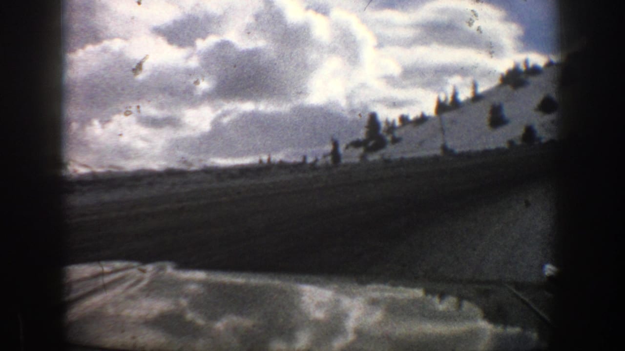 1961 Aspen home-movie view from inside a vehicle, looking past a snowy roadside hill and cloudy winter sky.