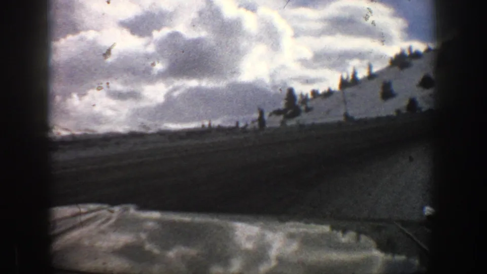 1961 Aspen home-movie view from inside a vehicle, looking past a snowy roadside hill and cloudy winter sky.