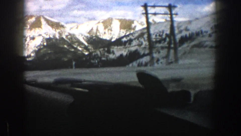 Aspen, Colorado winter road view from 1961 8mm footage, showing snowy mountains, utility poles, and car interior framing.