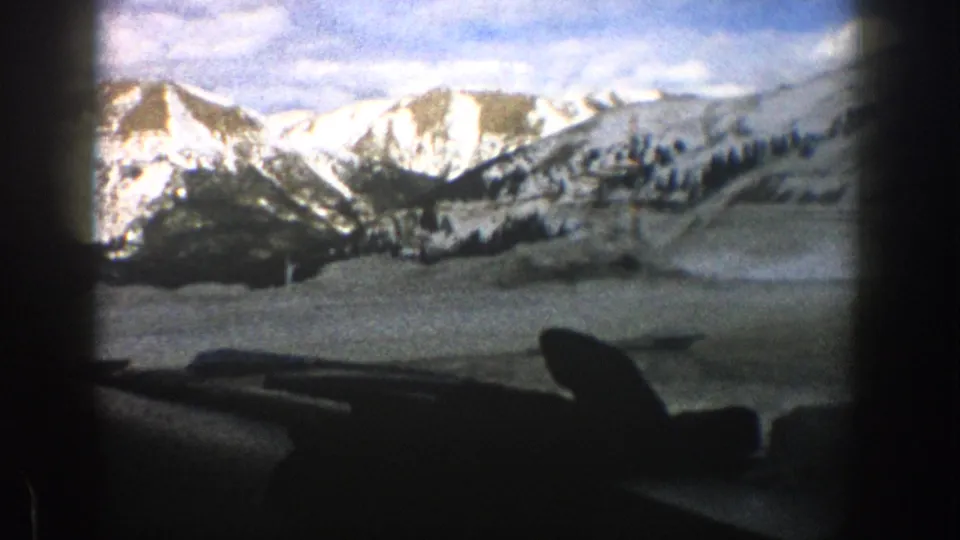 1961 Aspen 8mm frame of snow-covered mountains and hills seen from a moving vehicle interior.