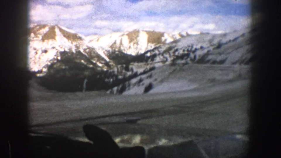 Aspen-area 8mm frame showing a snowy mountain landscape through a windshield, with dark dashboard and wiper forms in the foreground.