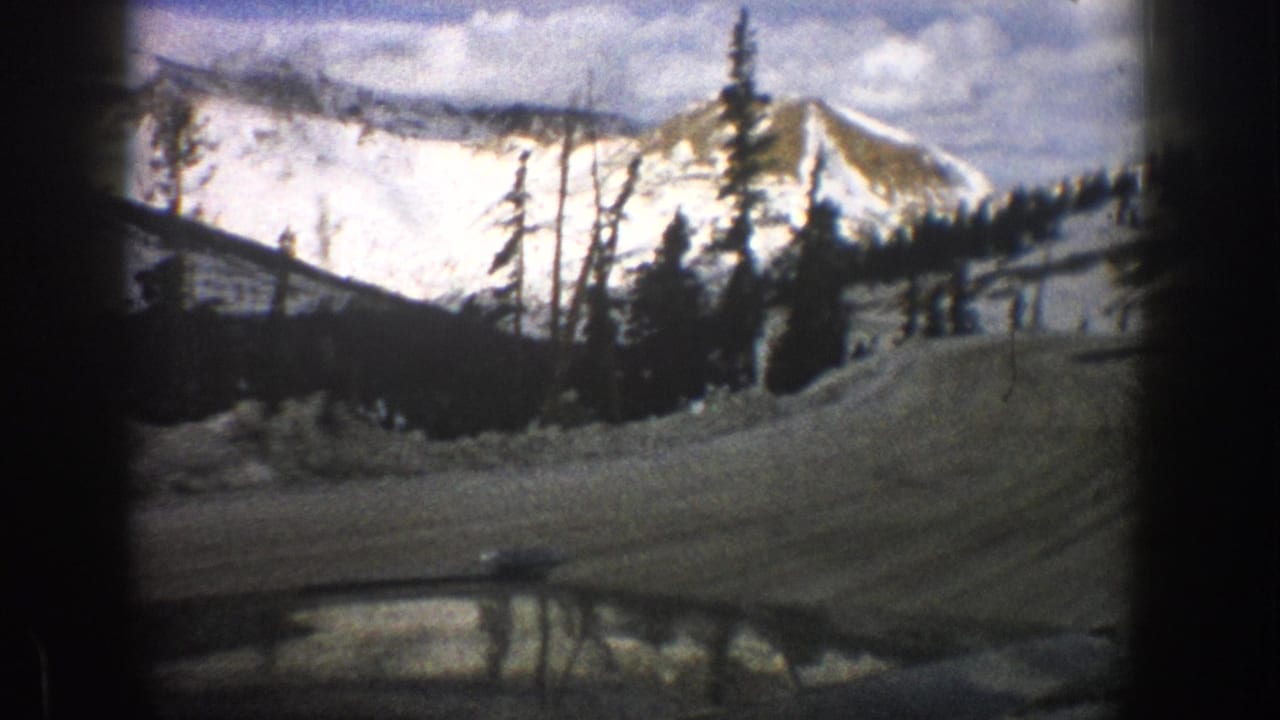 Aspen, Colorado 1961 home-movie frame showing a snowy mountain road from inside a car, with trees and peaks beyond.