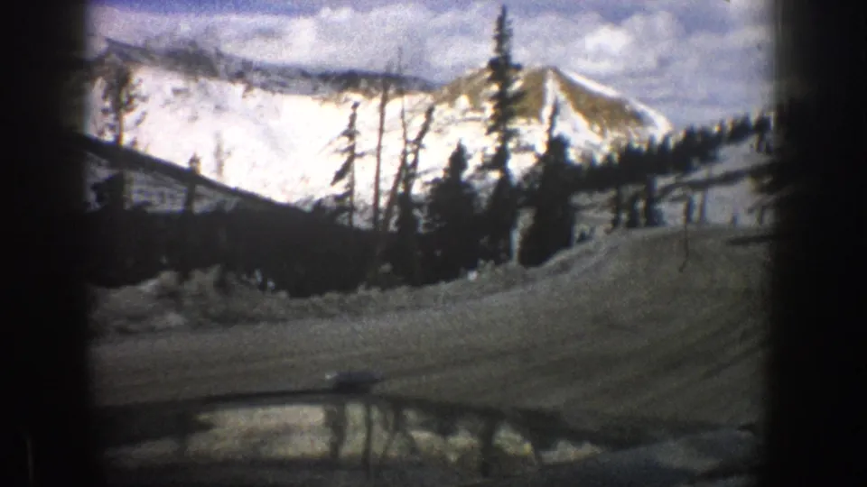 Aspen, Colorado 1961 home-movie frame showing a snowy mountain road from inside a car, with trees and peaks beyond.