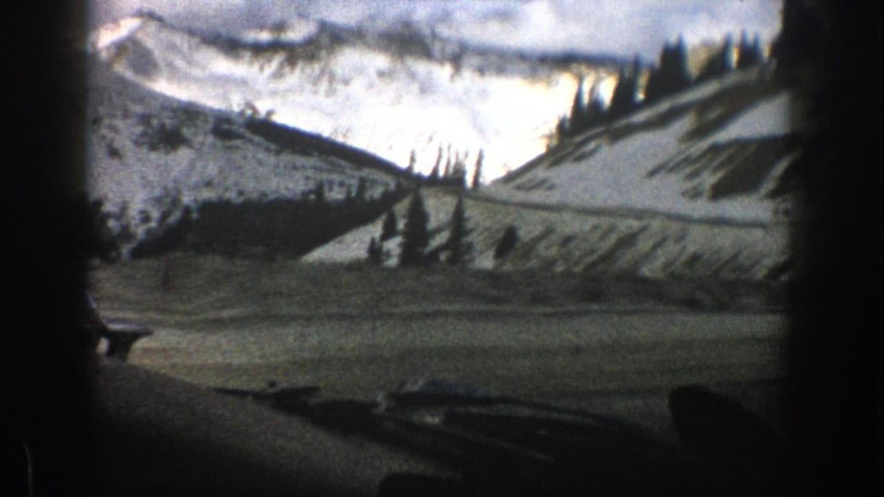Aspen, Colorado 8mm travel view with a snow-covered ridge, evergreen trees, distant peaks, and dark interior edges from a moving car.