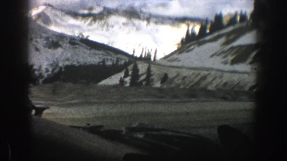 Aspen, Colorado 8mm travel view with a snow-covered ridge, evergreen trees, distant peaks, and dark interior edges from a moving car.
