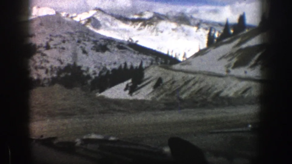 Final 1961 Aspen 8mm frame showing winter mountain scenery, evergreens, snowbanks, and the dark silhouette of the car interior.