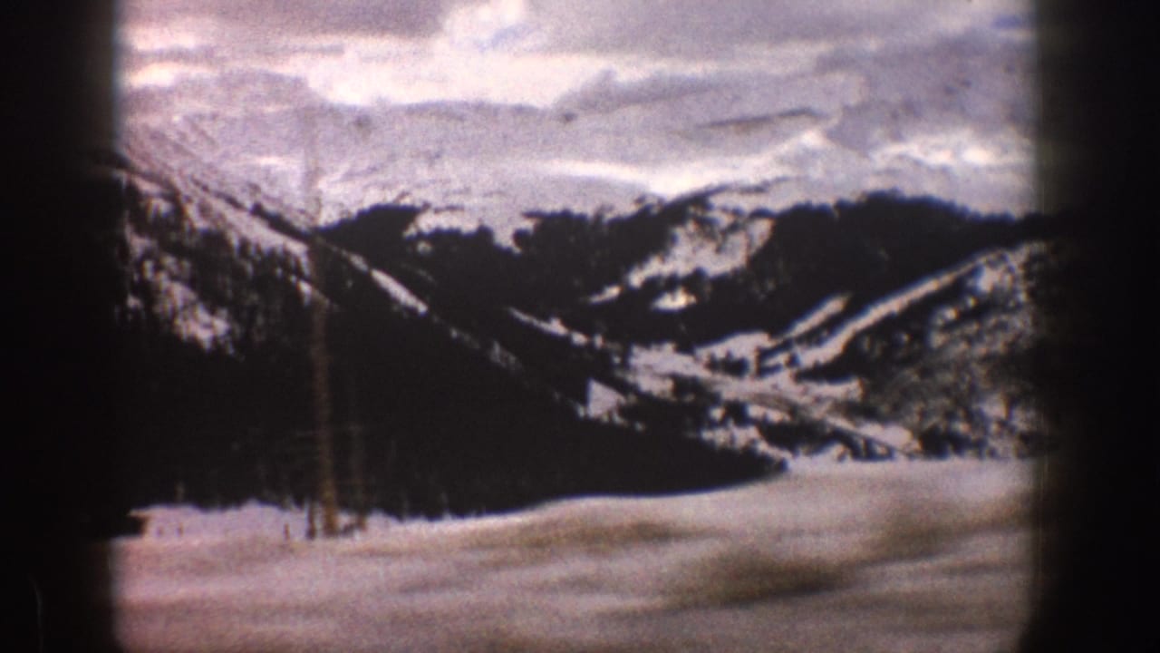 Snowy mountain valley with dark evergreen ridges under a cloudy sky.