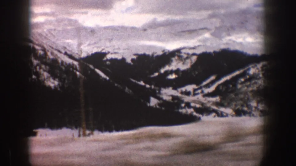 1961 Aspen, Colorado 8mm frame with a snowy mountain valley, dark tree-covered ridges, pale sky, and heavy vignette from the home-movie film frame.