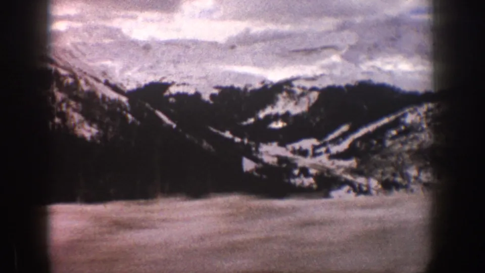 1961 Aspen, Colorado 8mm frame showing a snowfield foreground, dark evergreen-covered hills, distant white mountain slopes, and visible film-edge shadowing.
