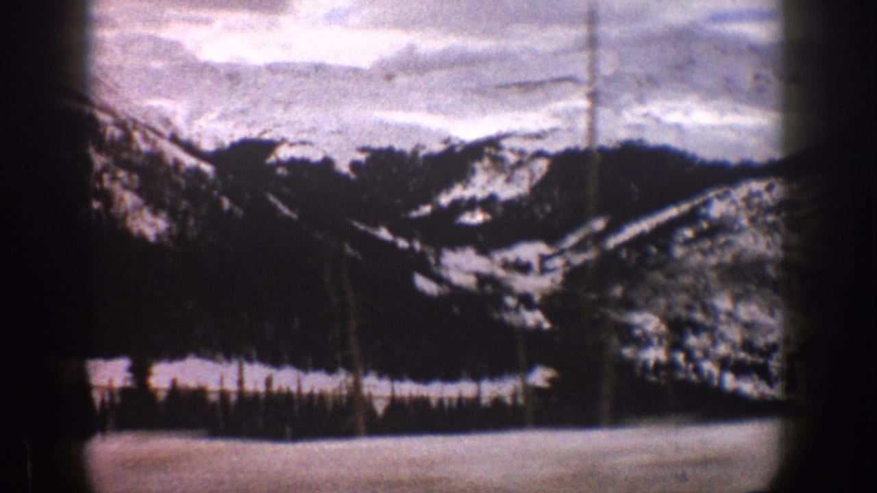 1961 Aspen-area 8mm frame showing snow-covered mountains, evergreen trees, and a pale winter foreground with heavy film-edge vignetting.