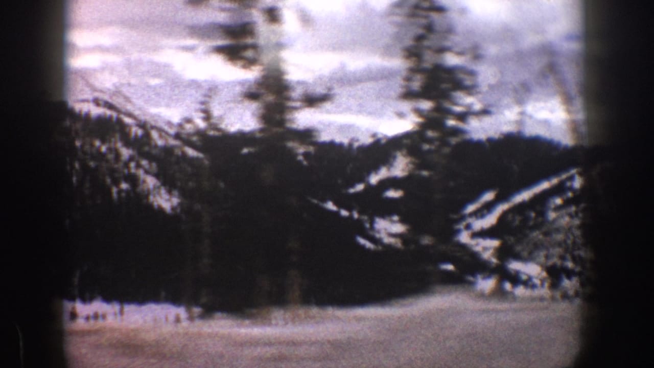 1961 Aspen-area winter view with snow-covered slopes, conifer trees, and an open snowy basin or field, softened by 8mm grain and vignetting.
