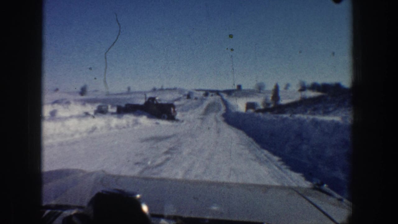 Moving 8mm car view near Aspen in 1961, showing a plowed snow road and a dark vintage truck beside open winter fields.