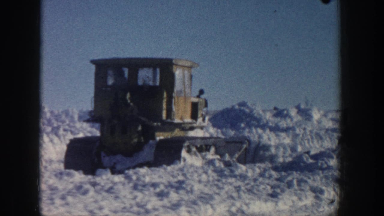 Boxy tracked plow beside piled snow on an open winter road.