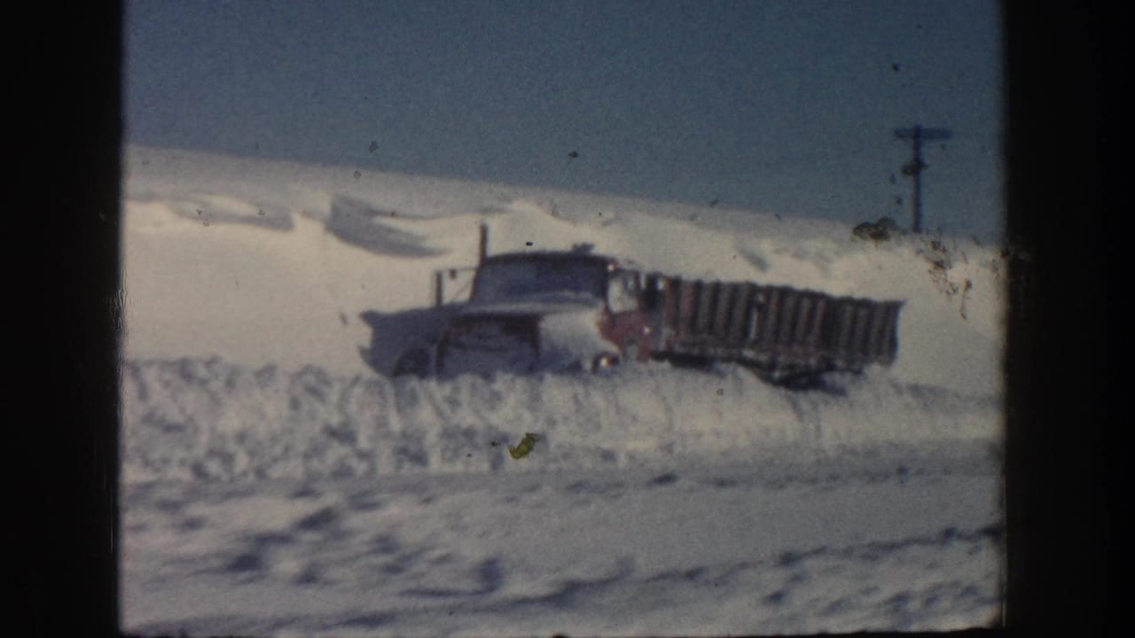 Truck and trailer stuck beyond a high bank of plowed snow.