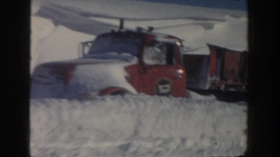 Close 8mm frame of a red-and-white truck cab buried up to the hood in Aspen snow, with the trailer extending behind it.