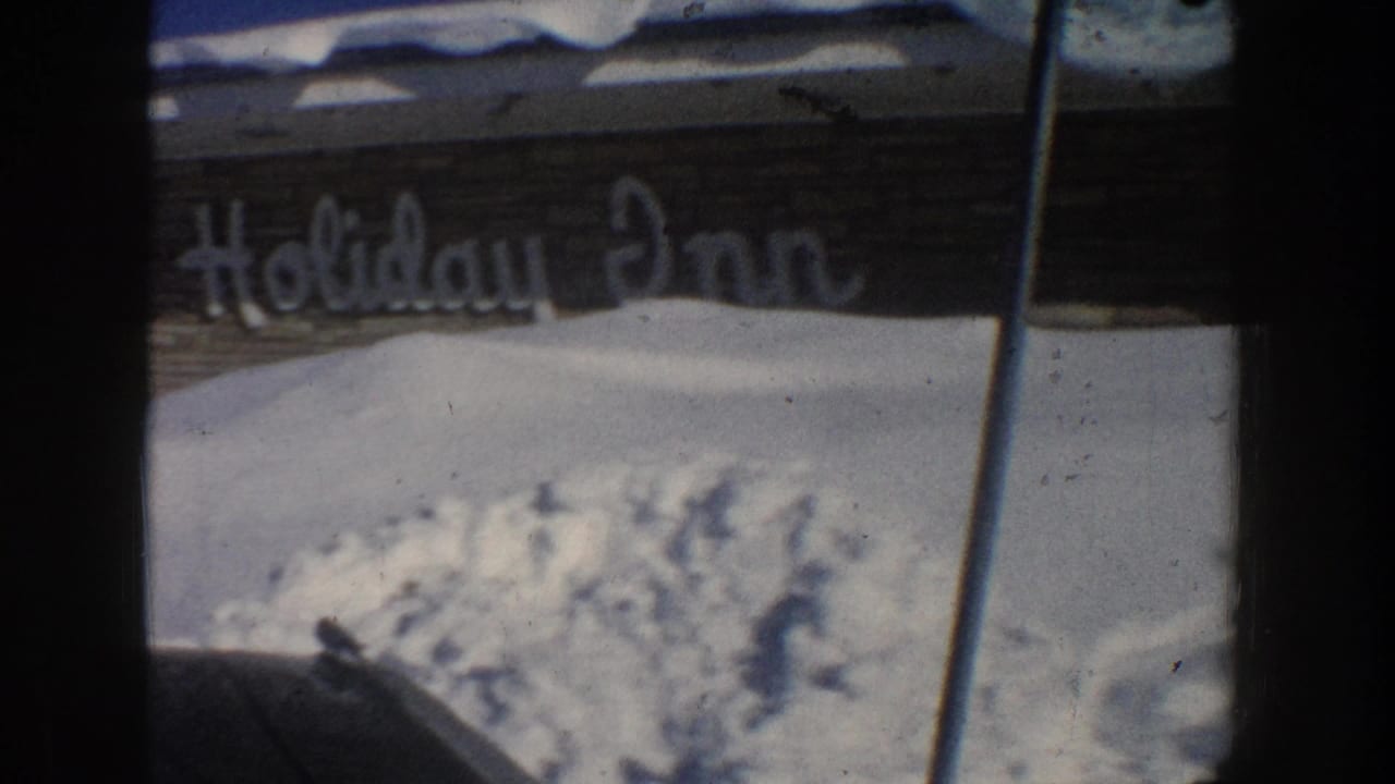 Holiday Inn sign partly visible above deep snowbanks beside a winter roadside building.
